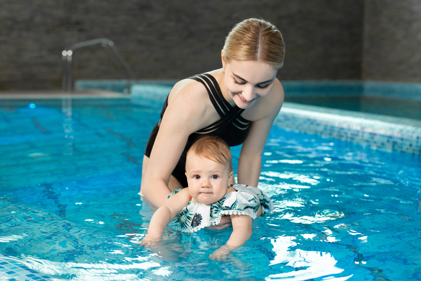 Swimming instructor teaching an infant to swim with a parent